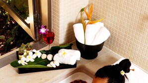 A bathtub filled with rose petals and flowers, a white towel, and a glass of red wine.