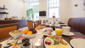 En frukostbuffé med ett varierat utbud av mat, en matsal med en avskild sittplats och ett kök i bakgrunden.