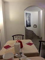 Un comedor con una mesa dispuesta para dos personas, con mantel blanco, servilletas rojas y un centro de mesa decorativo.