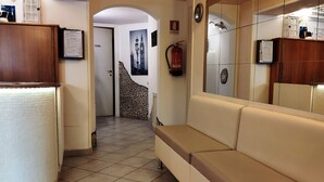 Um corredor com um sofá bege, piso de azulejos, parede de pedra e uma porta que dá para outro quarto.