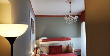 Habitación con literas, candelabro, lámpara y un cuadro en la pared.