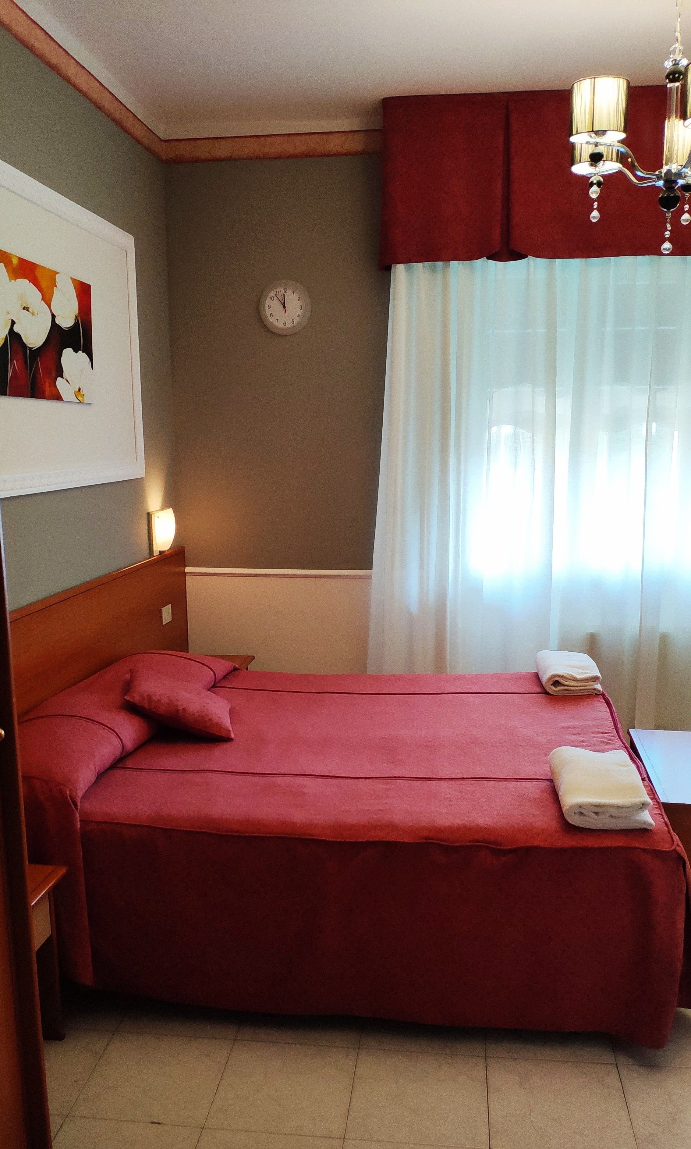 Habitación de hotel con cama, un reloj, un cuadro y una araña.