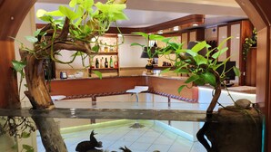 Uma área de bar com balcão de madeira, prateleiras com garrafas e um espaço de estar com uma cadeira branca.