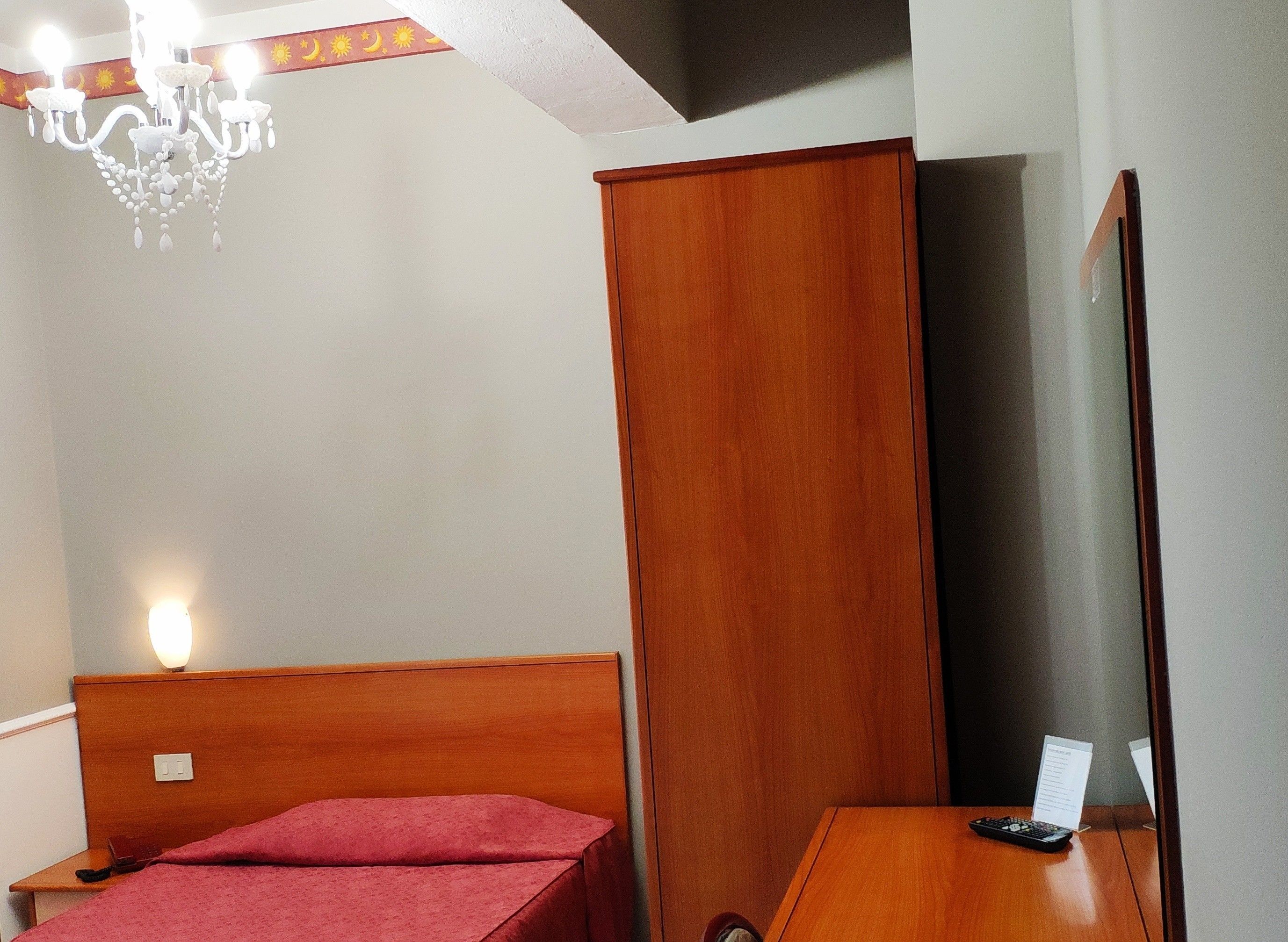 Habitación de hotel con una cama y un armario de madera, un espejo, una mesa con control remoto y un candelabro.