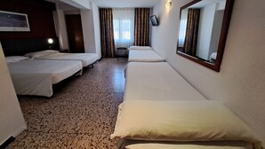 A hotel room with two single beds, a large mirror, a small table, and a window with curtains.