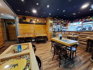 A restaurant interior with wooden walls, tables, chairs, a bar area, and a window with a view. - Cims (Pas de la Casa)