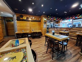 Interior de restaurante com paredes de madeira, mesas, cadeiras, balcão e uma janela com vista.