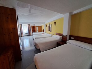 Een hotelkamer met vier bedden, een houten garderobe, een klein tafeltje en een spiegel.