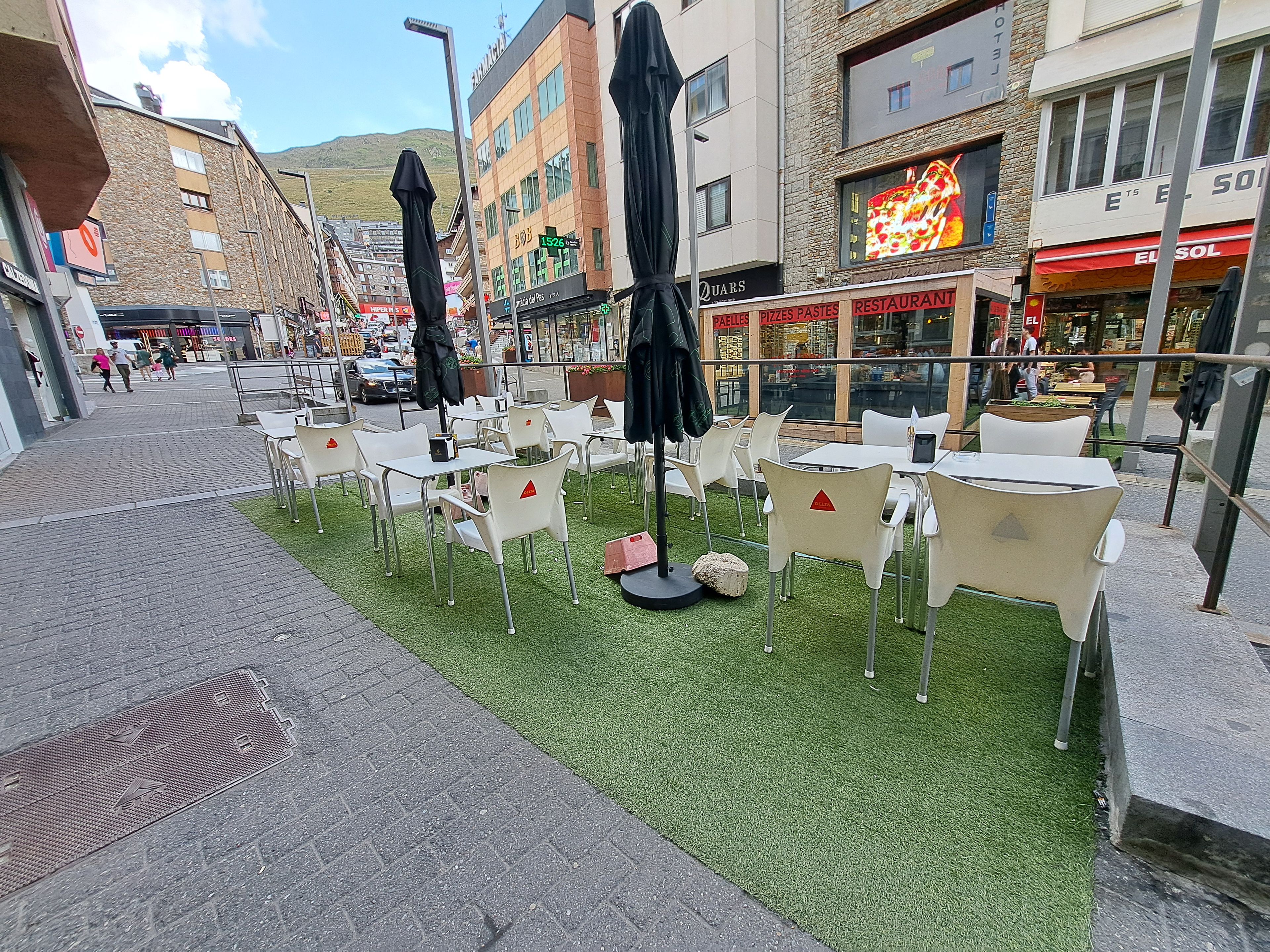 An outdoor seating area with tables and chairs, surrounded by buildings with various storefronts.