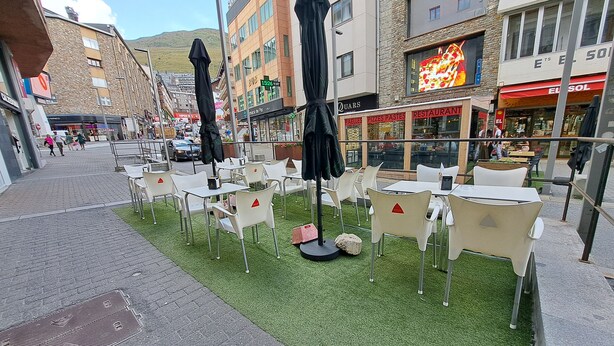 An outdoor seating area with tables and chairs, surrounded by buildings with various storefronts.