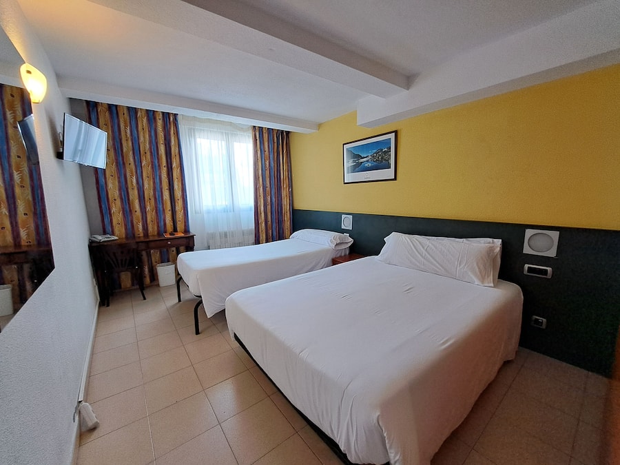 A hotel room with two beds, a desk, a chair, a television, and a window with curtains.