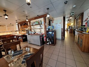 Un restaurant doté d’un bar, de tables et d’une cuisine que l’on peut apercevoir au fond de la salle.