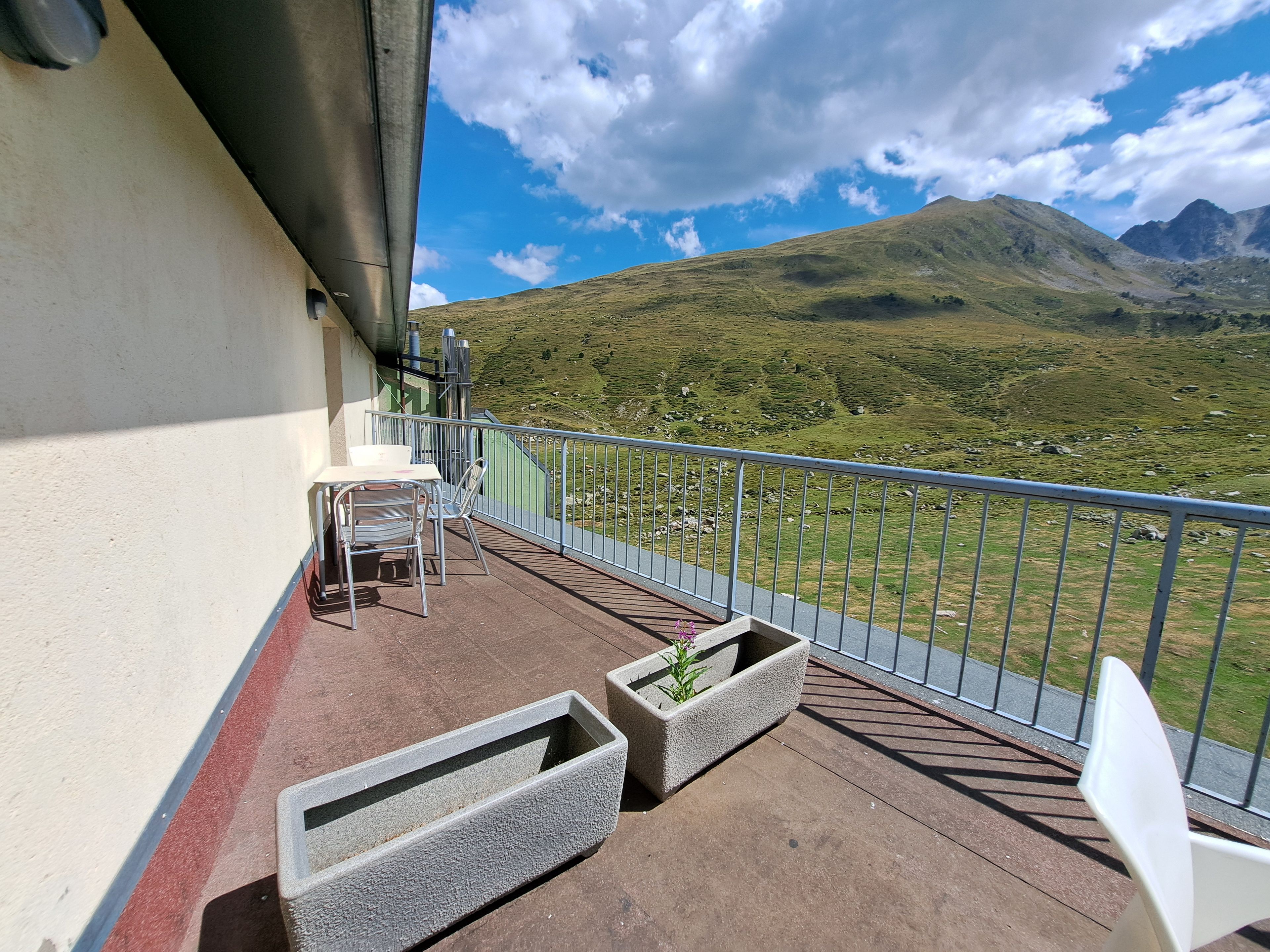 Un balcon avec une table et des chaises, une balustrade et une vue sur un paysage montagneux.