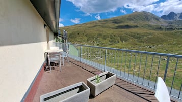 Un balcon avec une table et des chaises, une balustrade et une vue sur un paysage montagneux.