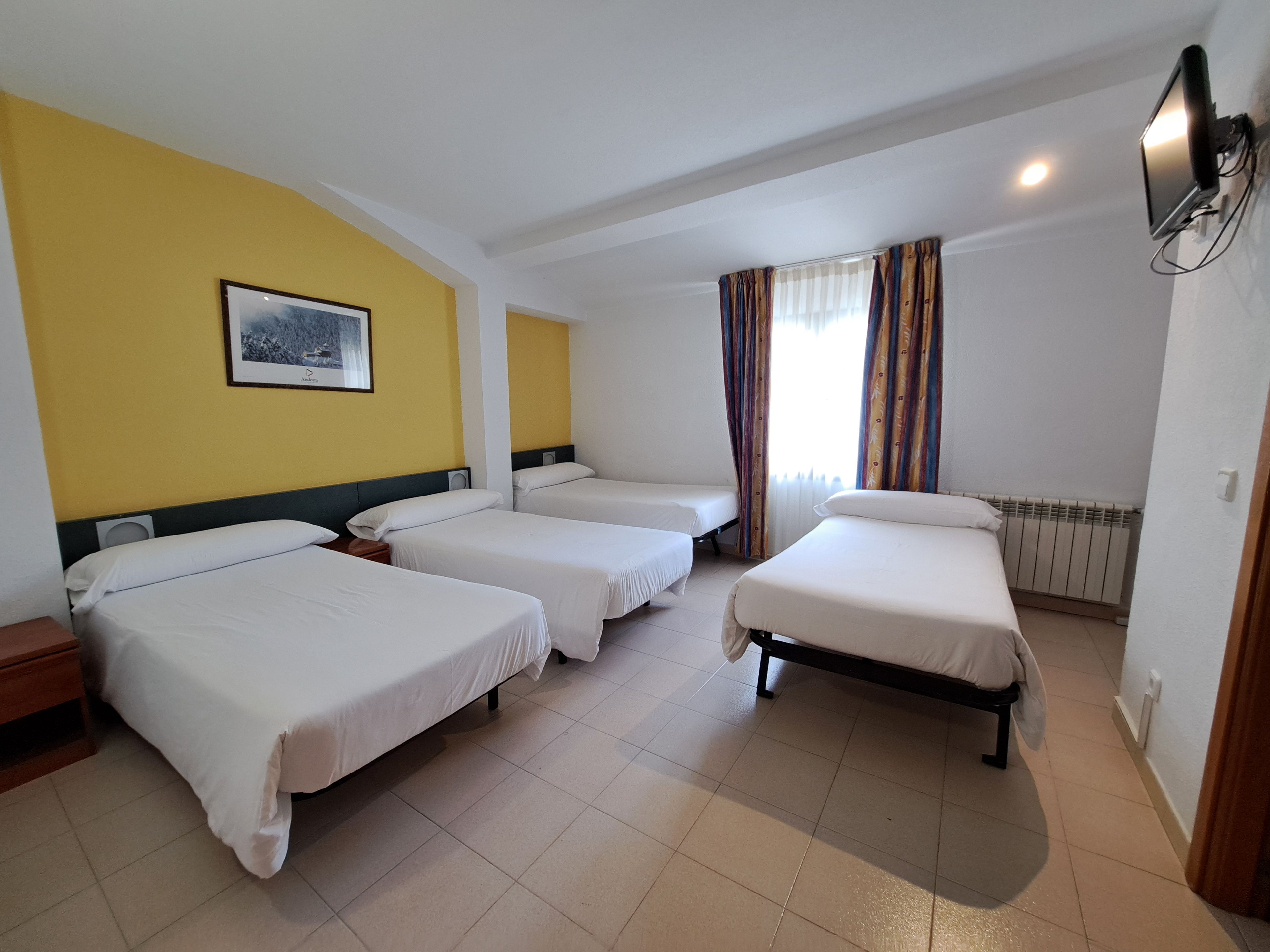 Een hotelkamer met drie enkele bedden, een groot raam met gordijnen, een wandtelevisie en een lijst met een afbeelding aan de muur.