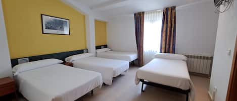 Habitación de hotel con tres camas individuales, un ventanal con cortinas, un televisor montado y un cuadro en la pared.