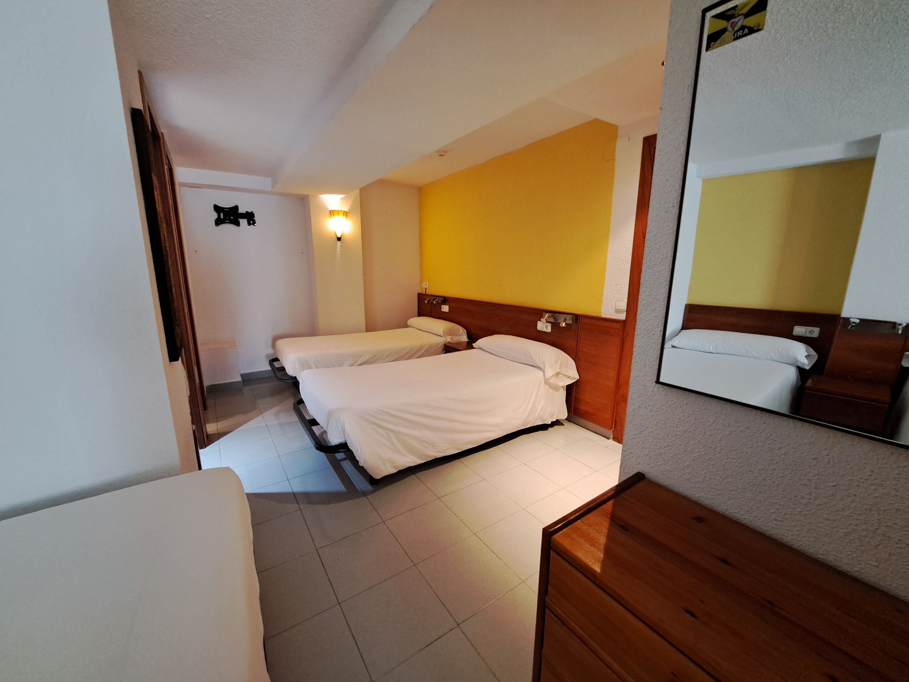 A hotel room with two beds, a wooden headboard, a mirror, and a wall-mounted light fixture.