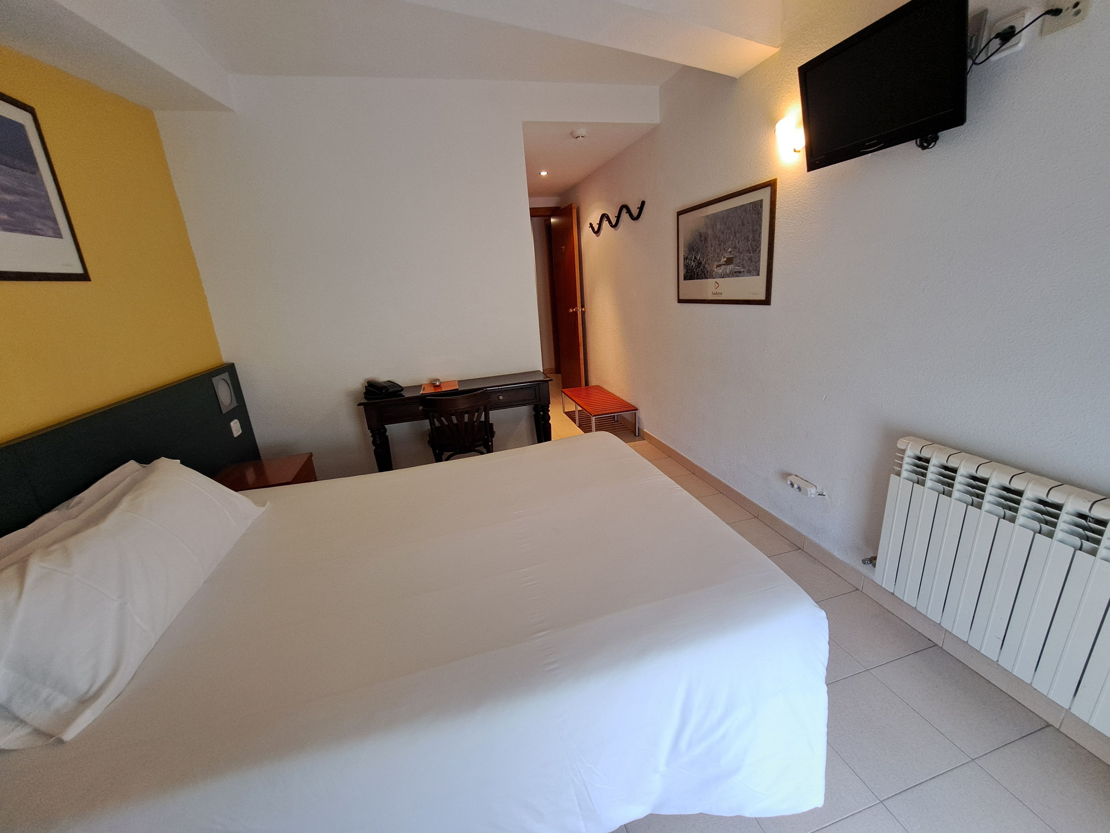 Habitació d'hotel amb llit, escriptori, cadira, televisió penjada a la paret i radiador.