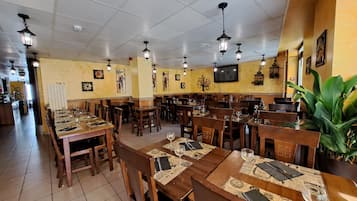 Un restaurante con varias mesas y sillas de madera, piso de baldosas y lámparas colgantes tipo farol.