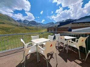 Une terrasse avec des chaises et des tables en plastique blanc, d’où l’on peut admirer un paysage montagneux.