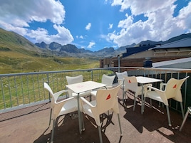 Una terraza con sillas y mesas de plástico blanco, con vistas a un paisaje montañoso.