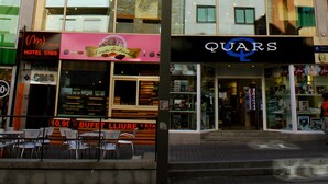 A hotel with multiple floors, signs for 'CHAMBRES' and 'HABITATIONS' indicating room availability, and a storefront with 'BUFFET' and 'LIURE' signs suggesting dining options.