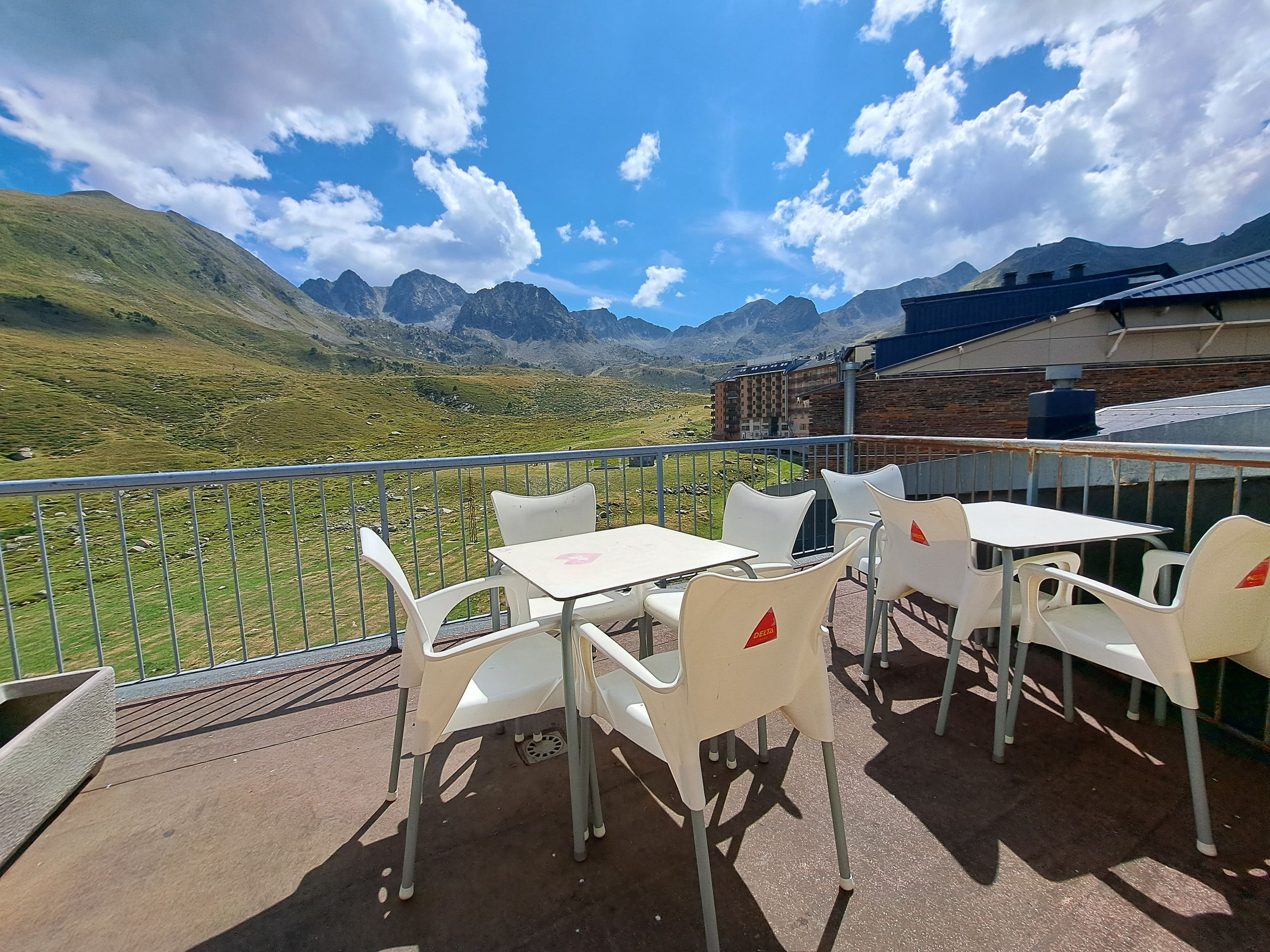 Eine Terrasse mit weißen Plastikstühlen und -tischen mit Blick auf eine Berglandschaft.