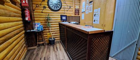 A wooden interior with a reception desk, a wall clock, a fire extinguisher, and a caution sign.