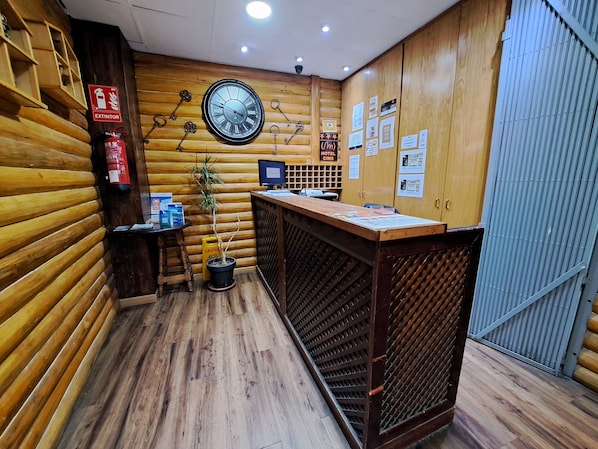 Interior de madera con un mostrador de recepción, un reloj de pared, un extintor y un letrero de precaución.