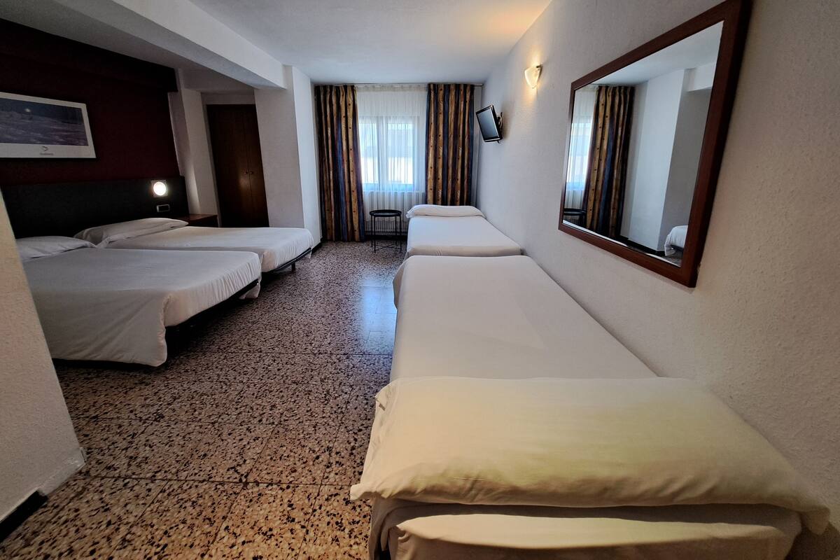 Habitación de hotel con dos camas individuales, un espejo grande, una mesita pequeña y una ventana con cortinas.