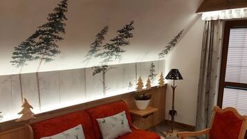 A cozy room with a red sofa, two wooden chairs, a small table, and a ceiling mural of trees.