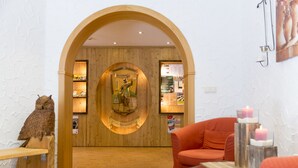 A reception area with a wooden archway, a reception desk, a plush orange chair, and a wall-mounted display. - Hotel und Restaurant Köhlerhütte (Gruenhain-Beierfeld)