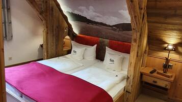 Ein hölzernes Himmelbett mit roter Decke, weißen Kissen und einer Landschaftsmalerei an der Wand dahinter.