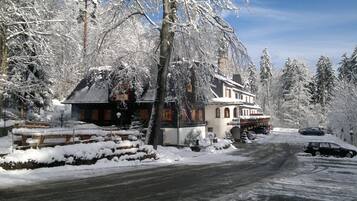 A snow-covered building with a traditional architectural style, a paved driveway, and parked cars.