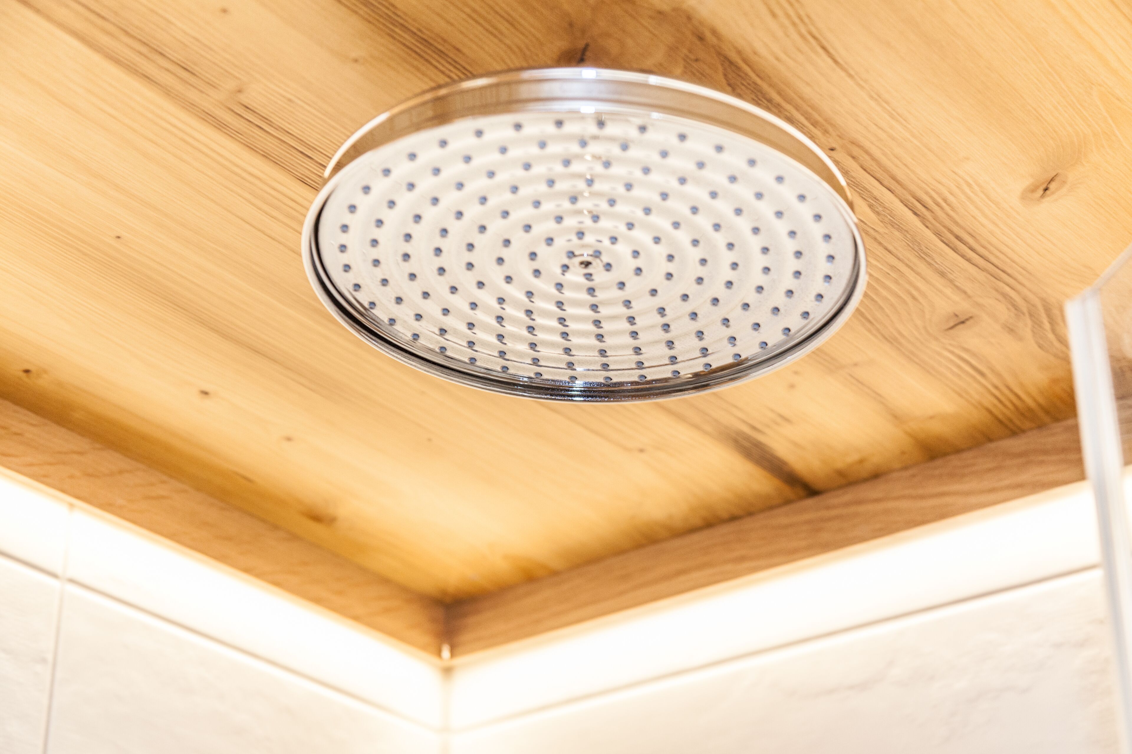 Un cabezal de ducha con diseño circular, sujeto a un techo de madera.