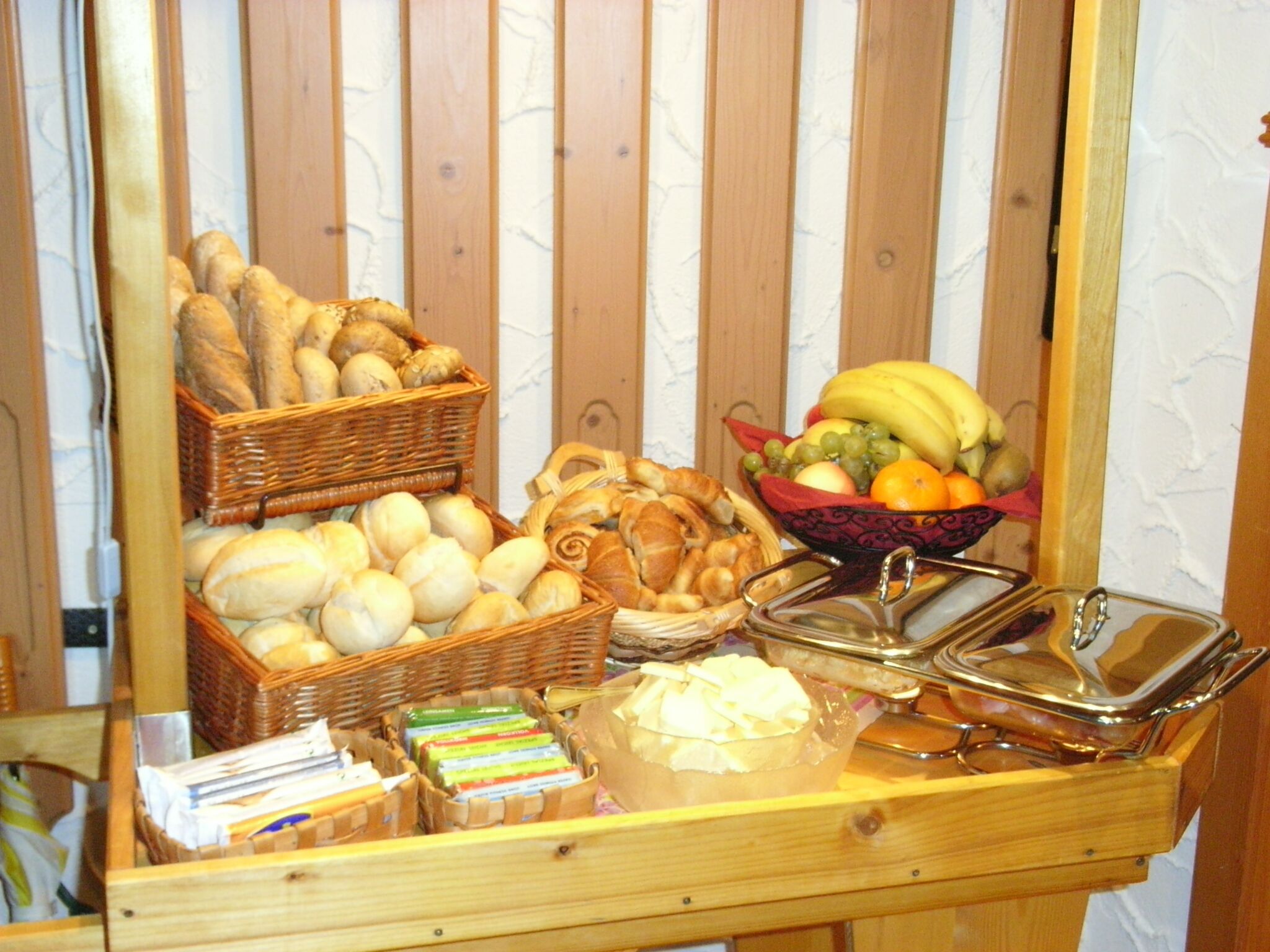 A breakfast buffet with bread, pastries, and a fruit bowl.
