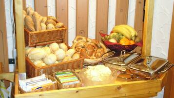A breakfast buffet with bread, pastries, and a fruit bowl.