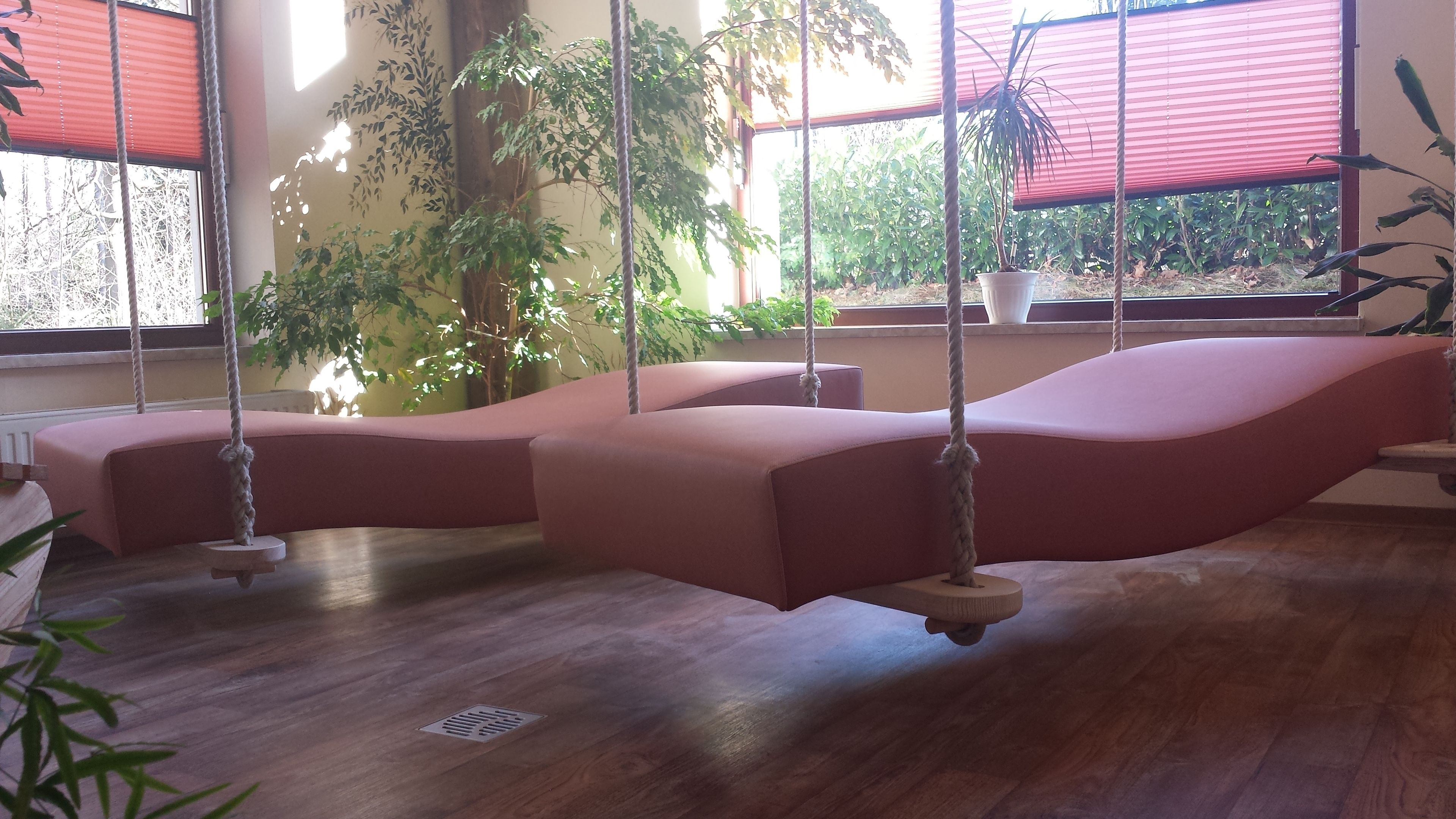 Una habitación con suelo de madera, sofá rosa y una silla mecedora.