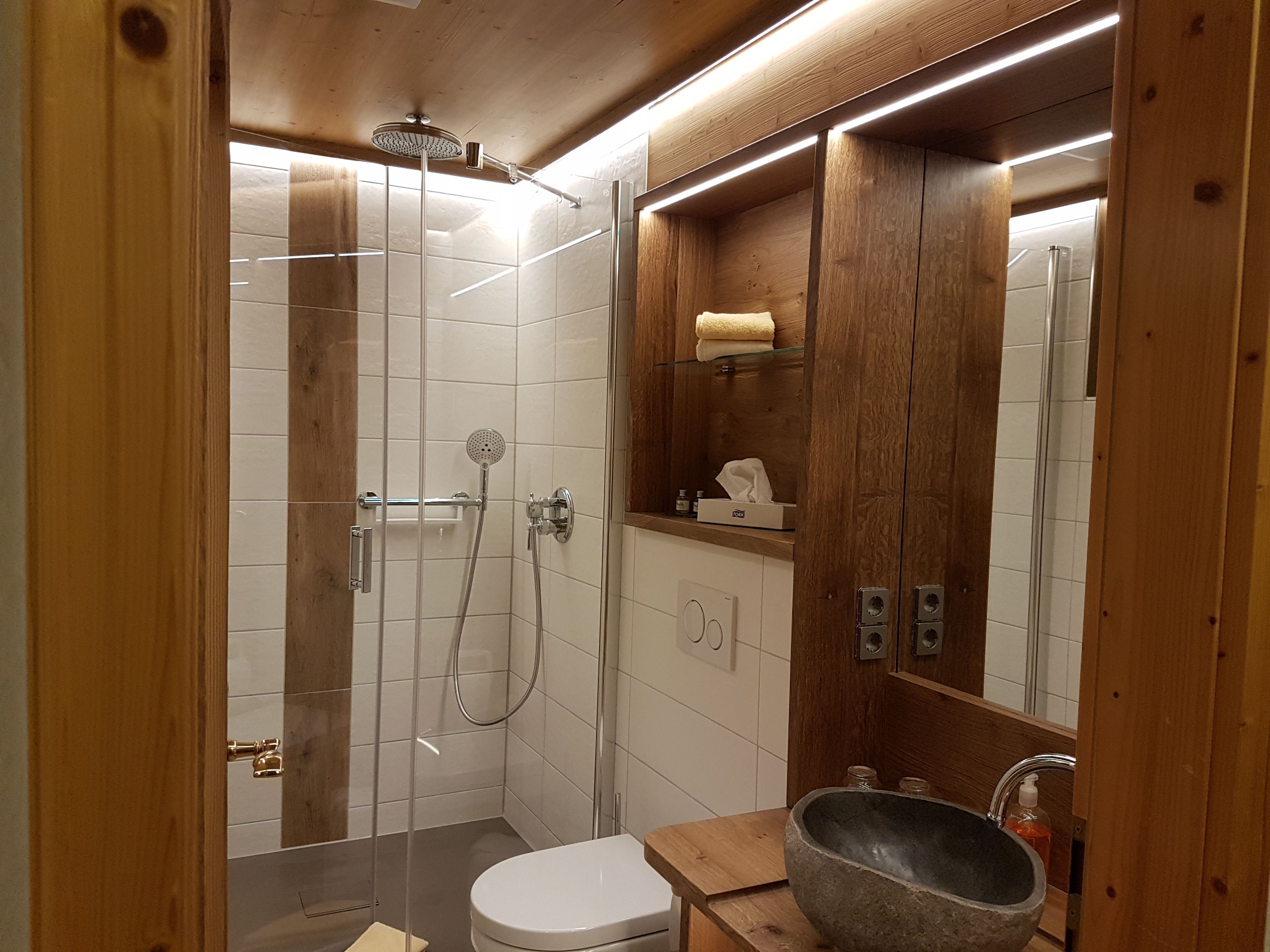 A modern bathroom with a glass-enclosed shower, a wooden vanity, and a large stone sink.