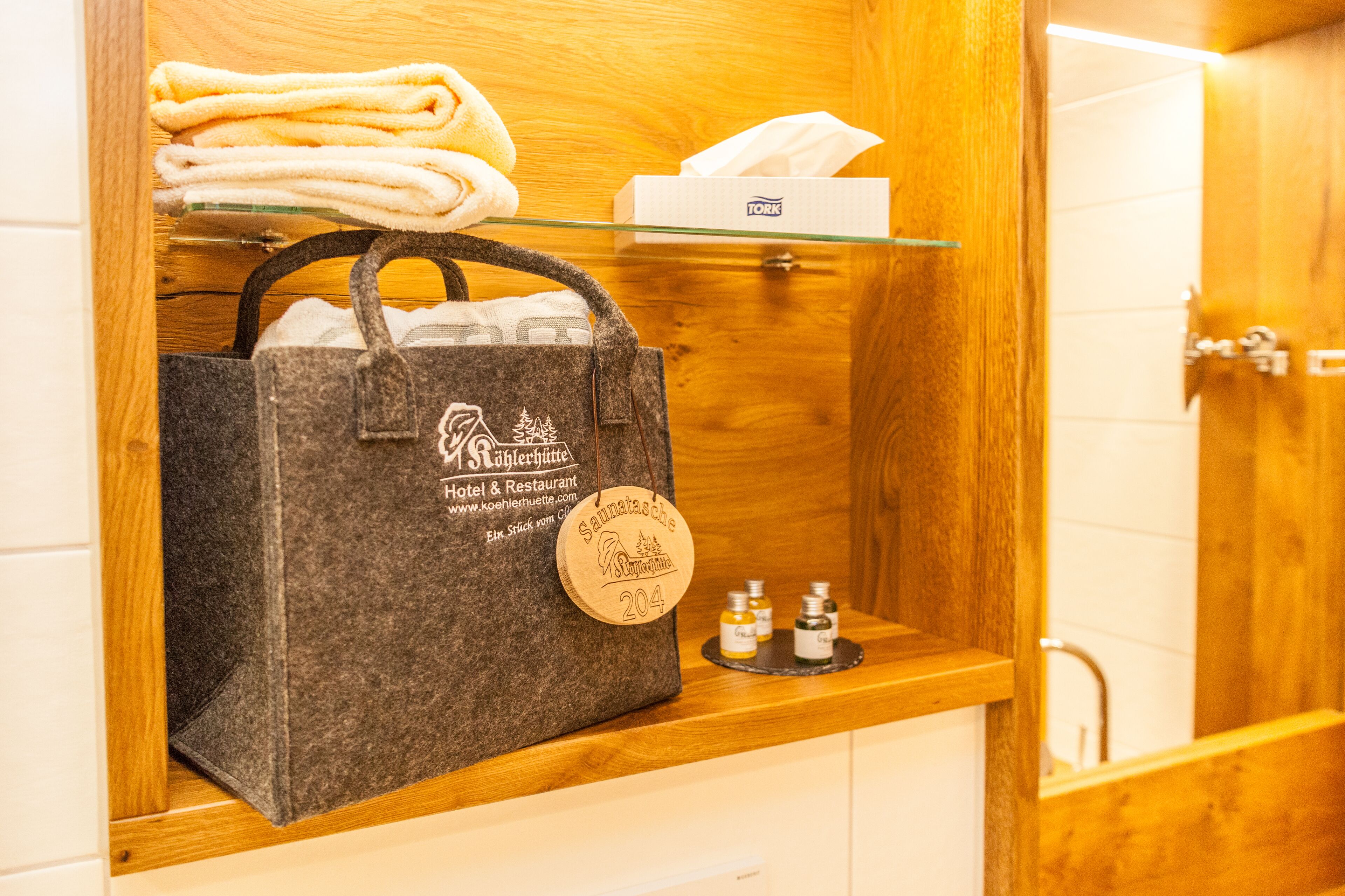 Un meuble en bois contenant une serviette pliée, une boîte de mouchoirs, un sac fourre-tout à l’effigie d’une marque et deux petites bouteilles.