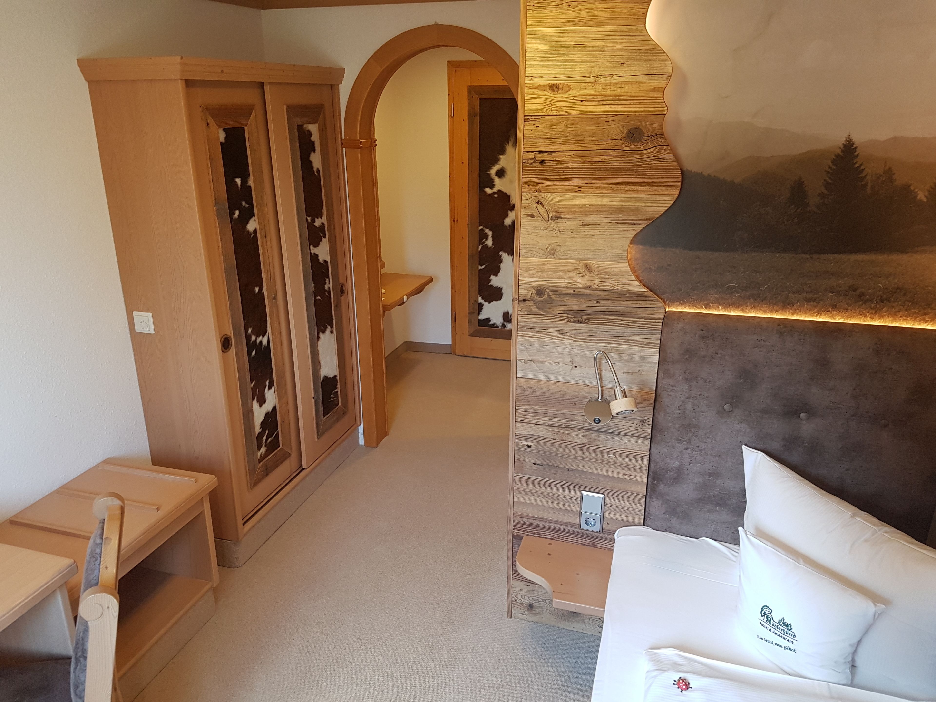 A cozy room with a wooden wardrobe, a small table, and a couch with a logo pillow.