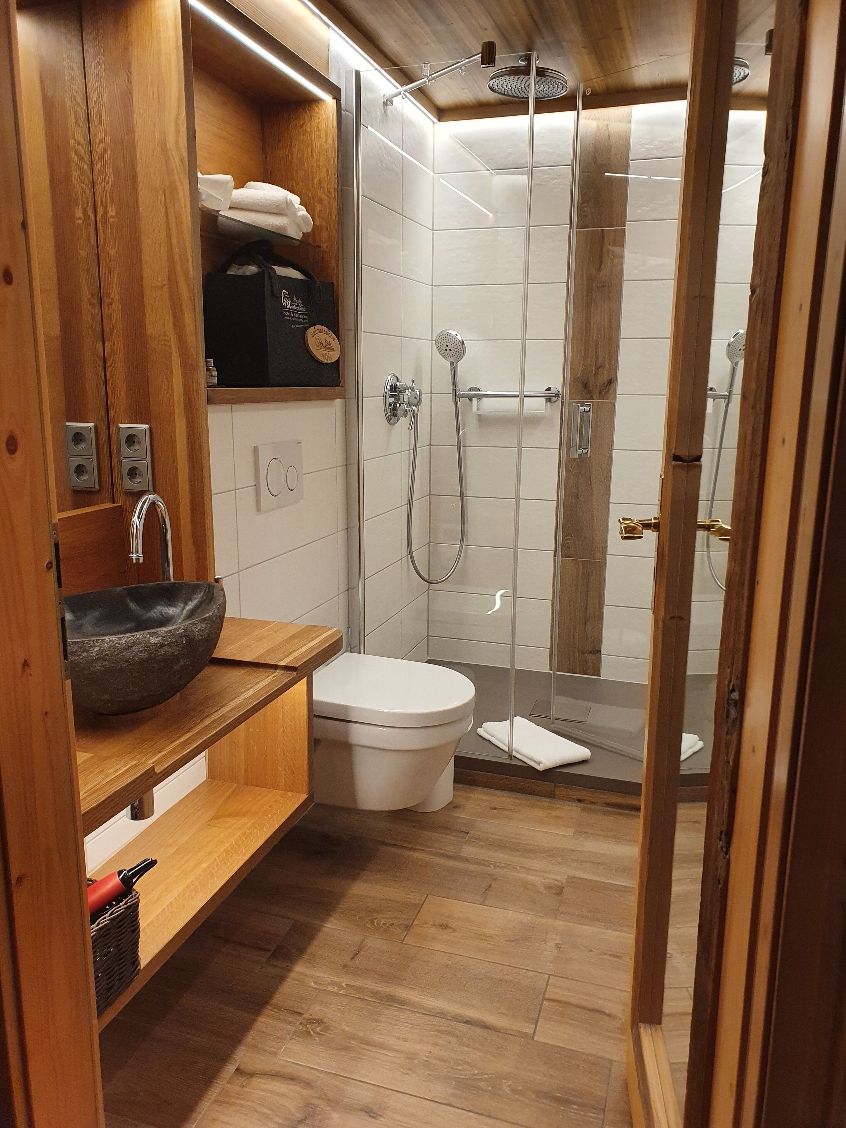 Uma casa de banho moderna com toucador de madeira, sanita branca e cabine de duche com vidro.