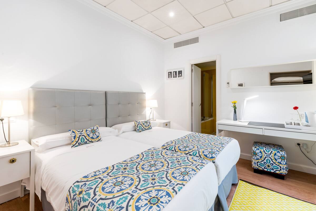 Ein Hotelzimmer mit einem großen Bett, Nachttischen, einem Schreibtisch und einem kleinen Hocker.
