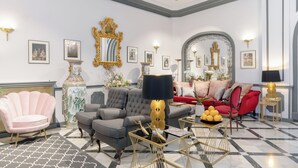 A well-appointed living room with a grey sofa, a red sofa, a pink armchair, a gold-framed mirror, and a large vase.