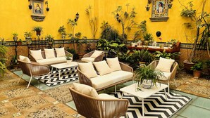 A yellow-walled patio with wicker furniture, potted plants, and decorative wall art.