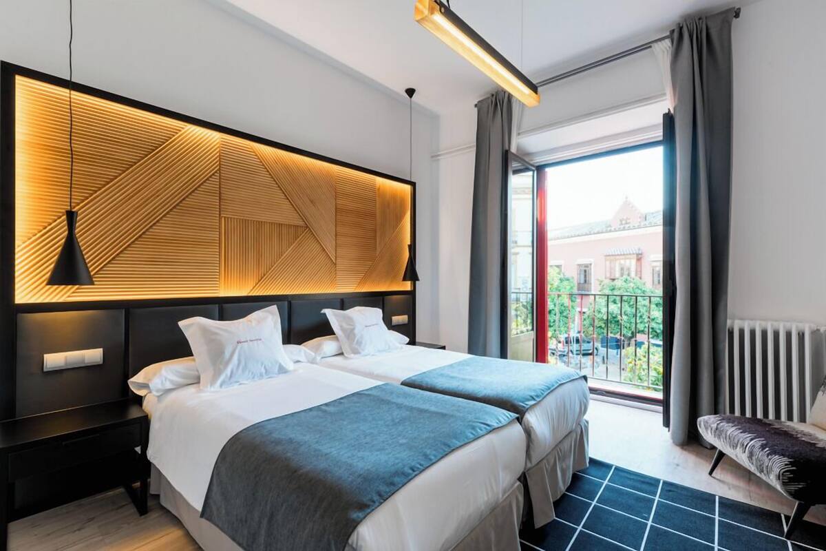 Ein Hotelzimmer mit zwei Betten, einem großen Fenster mit Blick, einem modernen Kopfteil und einer Bank am Fenster.