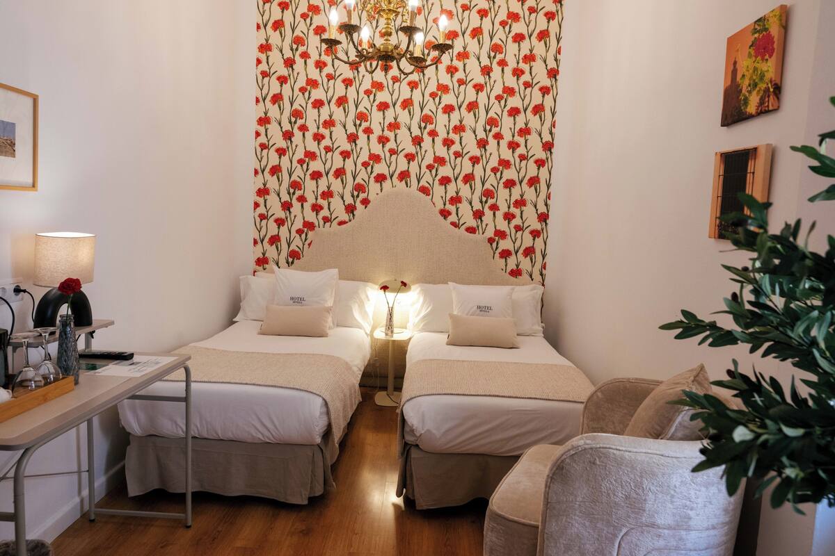 Ein Hotelzimmer mit zwei Betten, einem Schreibtisch, einer Lampe und einem Kronleuchter.