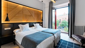 A modern hotel room with two beds, a geometric-patterned headboard, a view of the city, and a balcony with a view of buildings.