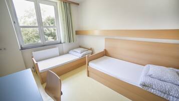Ein kleiner, sauberer Raum mit einem Etagenbett, einem Einzelbett, einem Schreibtisch und einem Fenster mit Vorhängen.