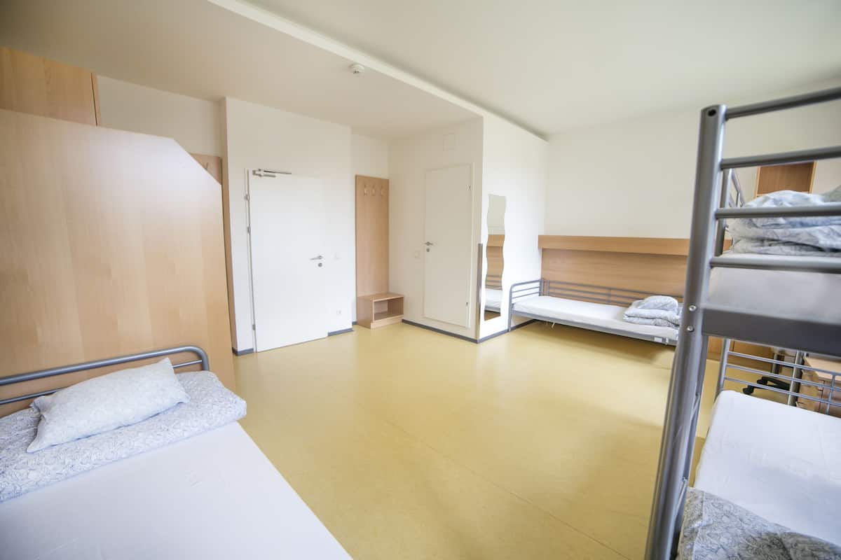 A hotel room with a bunk bed, a single bed, and a wooden wardrobe.